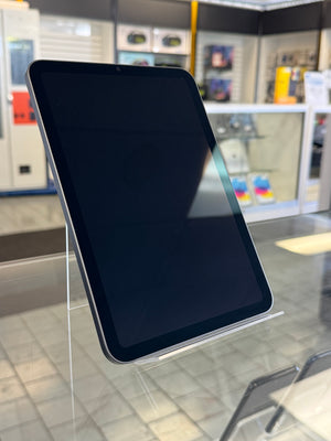 A black tablet device with a glossy screen, displayed on a clear acrylic stand inside a retail store.