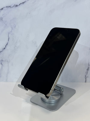 A silver metal phone stand holding a black smartphone, set against a white marble-patterned background.