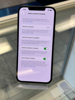 A black smartphone displaying the iOS Battery Health & Charging settings screen, photographed from above on a reflective glass surface.