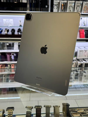 A silver Apple iPad Pro shown from the back, resting on a display stand inside a retail store with watch and accessory displays visible in the blurred background.