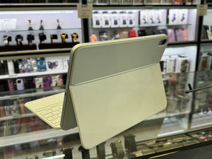 A light beige or cream-colored tablet case with an attached keyboard cover, shown standing open on a glass display counter inside a retail store.
