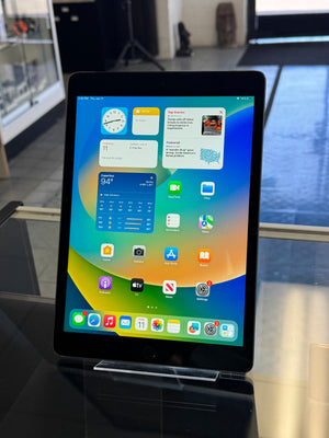 Tablet computer displaying a colorful home screen with various app icons in an indoor setting.