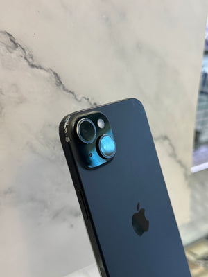 A close-up of the back of a black Apple iPhone showing the camera lenses and Apple logo, resting on a light marble surface.