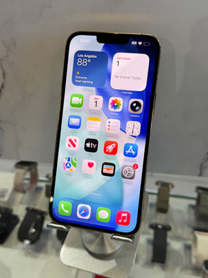 A black Apple iPhone with a lit screen displaying the home screen, resting on a silver metal display stand in a retail setting.