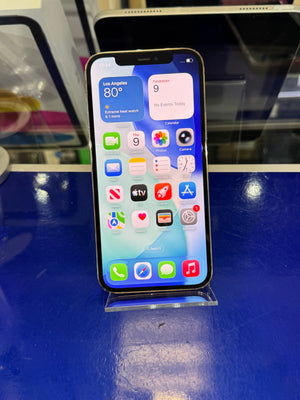 An iPhone with a lit home screen displaying various apps, resting on a clear plastic display stand on a glossy blue counter.