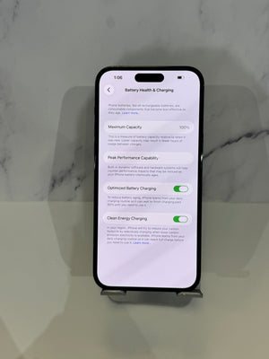 A black smartphone displayed upright on a small stand against a light gray marble-patterned background. The phone screen is on and showing the Battery Health & Charging settings page.