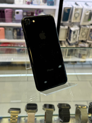 Black smartphone on a clear stand with shelves of electronic products in the background
