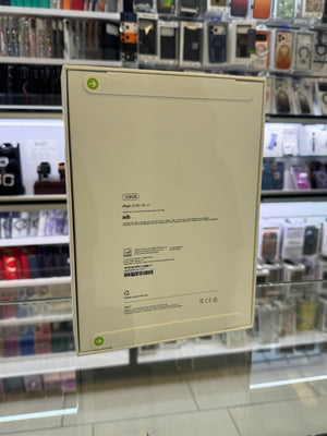 The back of a white Apple iPad packaging box, showing product specifications and barcodes, set against a blurred retail store background.