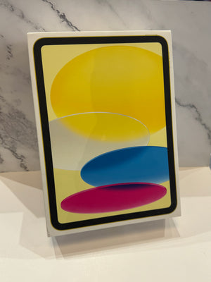 An Apple iPad box shown from above on a white marble surface, with the screen displaying a yellow, blue, and pink abstract wallpaper.
