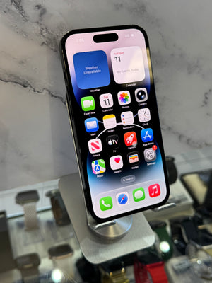 A black iPhone with its screen on, displaying the home screen, resting on a silver metal display stand in front of a gray marble-patterned background.