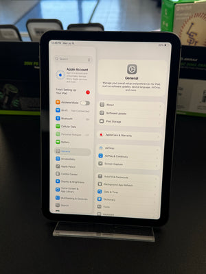 An iPad displaying the Settings app on a clear stand, photographed indoors with a blurred office or retail background.