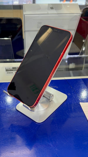A red smartphone with a black screen, displayed on a silver stand on a blue counter in a retail store.