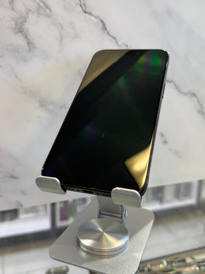 A black smartphone with a glossy screen resting on a silver metal stand, set against a white marble-patterned background.