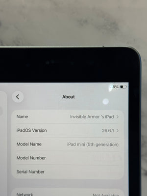 A close-up of a tablet screen showing the iPadOS About page with device details, set against a light marble-like background.