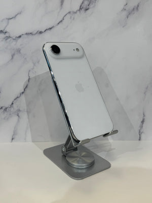 A silver Apple iPhone with a white back is displayed on a metallic silver adjustable stand against a white marble-patterned background.