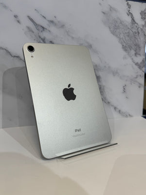 A silver Apple iPad shown from the back, standing upright on a clear display stand against a white marble-patterned background.