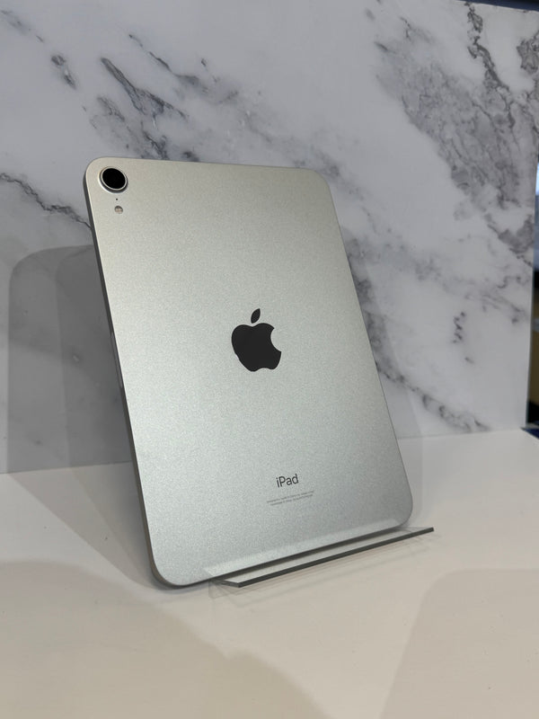 A silver Apple iPad shown from the back, standing upright on a clear display stand against a white marble-patterned background.
