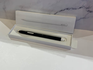 Apple Pencil Pro in black inside its original white packaging box, set against a white surface with a gray marble-patterned background.