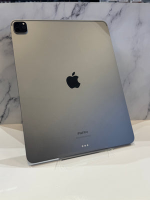 The back of an Apple iPad Pro in a metallic finish, standing upright on a clear display stand against a white marble-patterned background.