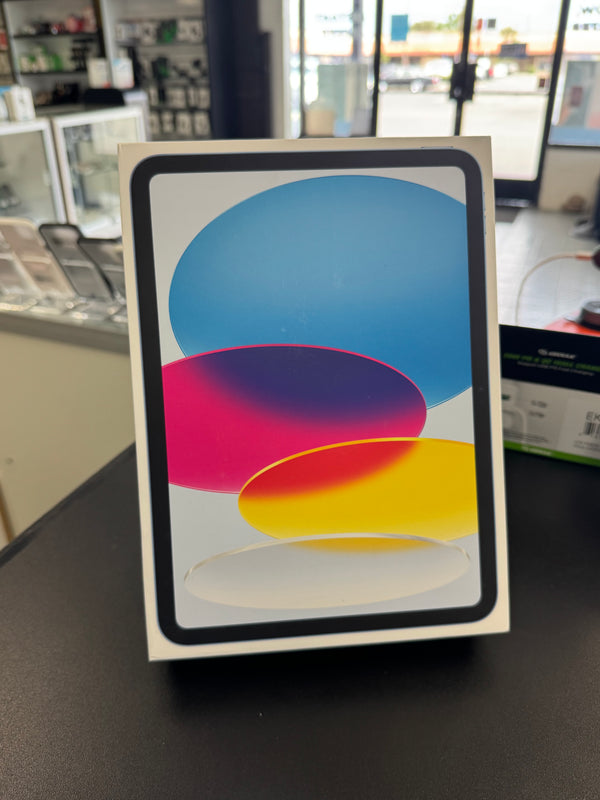 An Apple iPad box standing upright on a dark countertop in a retail store setting. The front of the box shows the iPad screen with a colorful abstract wallpaper featuring blue, pink, purple, and yellow shapes.