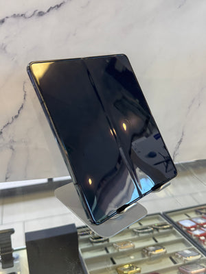 A black foldable smartphone displayed on a metallic stand inside a retail store, with a marble-patterned wall and jewelry display cases in the background.