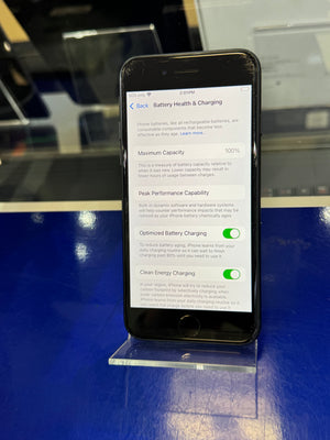 Smartphone displaying battery health and charging settings on a reflective surface