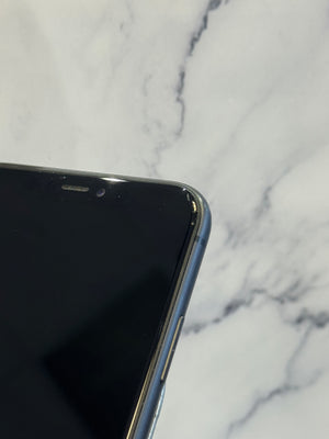 Close-up of the top-left corner of a smartphone with a black screen and metallic edge, resting on a white marble surface.
