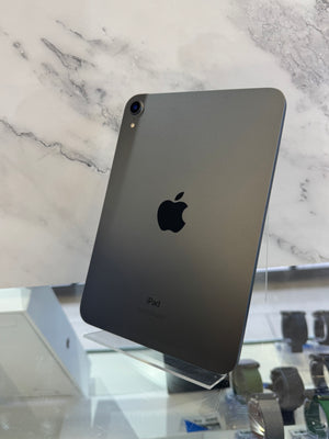 A dark gray Apple iPad shown from the back, standing on a clear display stand in front of a white marble-patterned background.