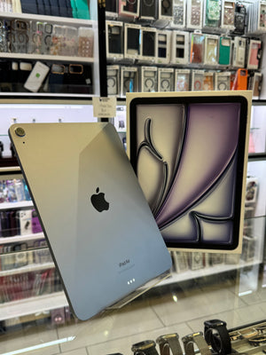 An Apple iPad Pro shown in a retail store setting, with the back of the silver device leaning against its original box on a glass display counter. The background is filled with shelves of phone cases and accessories.