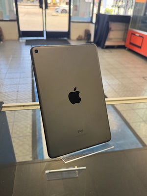 An Apple iPad with a dark gray backplate and the iconic black Apple logo, displayed on a stand inside what appears to be a store or office.