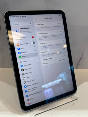 An iPad displaying the Settings app, with the Battery tab open, photographed on a clear acrylic stand against a light gray marble-like background.