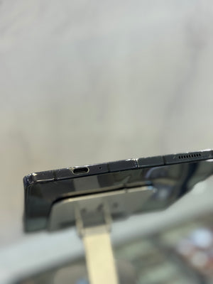 Close-up of the side edge of a black smartphone mounted on a display stand, showing the USB-C port and speaker grille against a blurred light gray background.