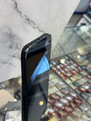 A black smartphone lying on its side on a white marble surface, with a blurred retail display in the background.