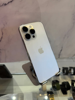 A silver Apple iPhone Pro showing its back panel with the triple-camera system and Apple logo, displayed on a stand in front of a marble-patterned wall.