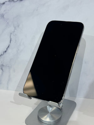 A silver smartphone with a black screen resting on a metallic silver stand, set against a white marble-patterned background.