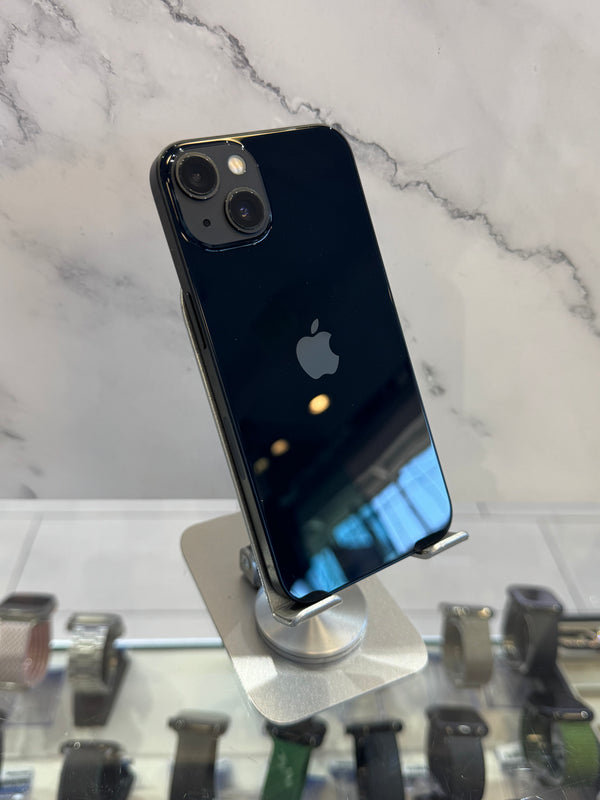 A black Apple iPhone 12 Pro displayed on a silver metal stand, showing its rear camera lens and the Apple logo against a marble-patterned background.