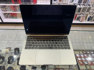 A silver aluminum laptop with a black screen and black keyboard, displayed on a glass retail counter with watches and accessories in the background.