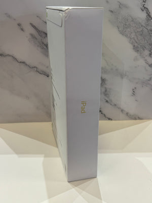 A tall, slim white iPad retail box standing upright, showing the side panel with the gold 'iPad' logo, set against a white marble-patterned background.
