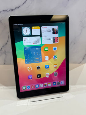 A black Apple iPad tablet standing upright on a clear display stand against a white marble-patterned background.