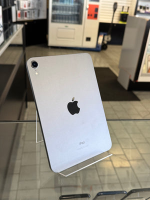 A silver Apple iPad tablet standing upright on a clear display stand inside a retail store, with the Apple logo visible on the back.