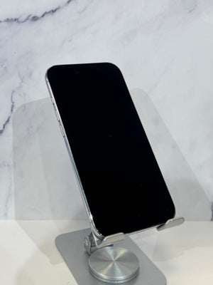 A silver aluminum phone stand holding a black smartphone, set against a white marble-patterned background.
