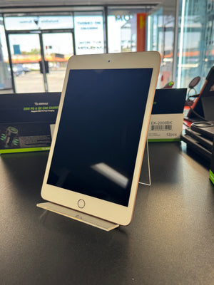 A gold-colored tablet with a black screen, displayed on a clear acrylic stand on a dark countertop inside a store.