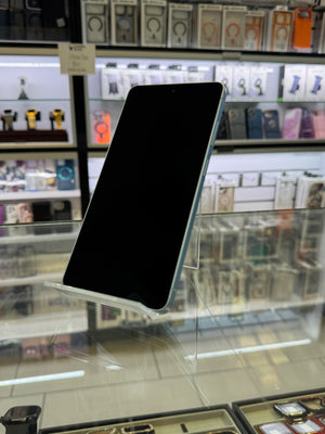 A black smartphone with a light blue side frame displayed on a clear stand inside a retail store, with shelves of phone accessories and boxes visible in the background.