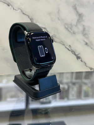A black Apple Watch with a dark gray fabric sport band resting on a black charging dock, set against a marble-patterned background.