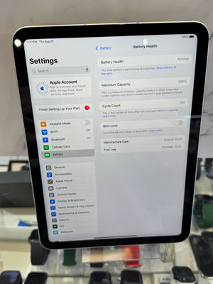 A black iPad displaying the Settings app on its screen, photographed indoors with a blurred retail or office background.