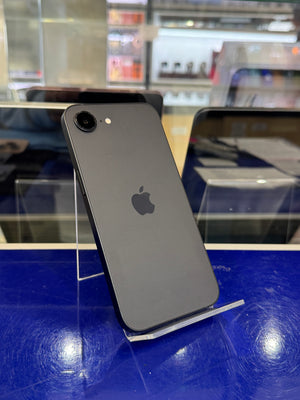 A dark gray Apple iPhone shown from the back, resting on a clear display stand against a bright blue counter in a retail setting.