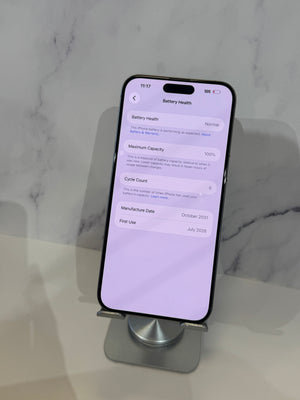 A black smartphone displayed upright on a small metallic stand against a light marble-patterned background. The phone screen is on and showing the Battery Health settings page.