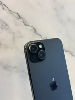 A close-up of the back of a dark gray or black Apple iPhone resting on a white marble surface.