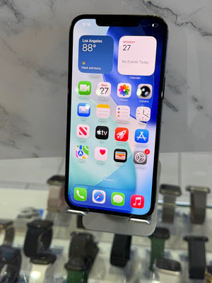A black smartphone with a large front-facing display showing various app icons, photographed from above on a light marble-like surface with blurred retail fixtures in the background.