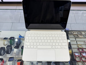 A white wireless keyboard and trackpad combo attached to a silver laptop with a black screen, displayed on a glass retail counter with watches in the background.